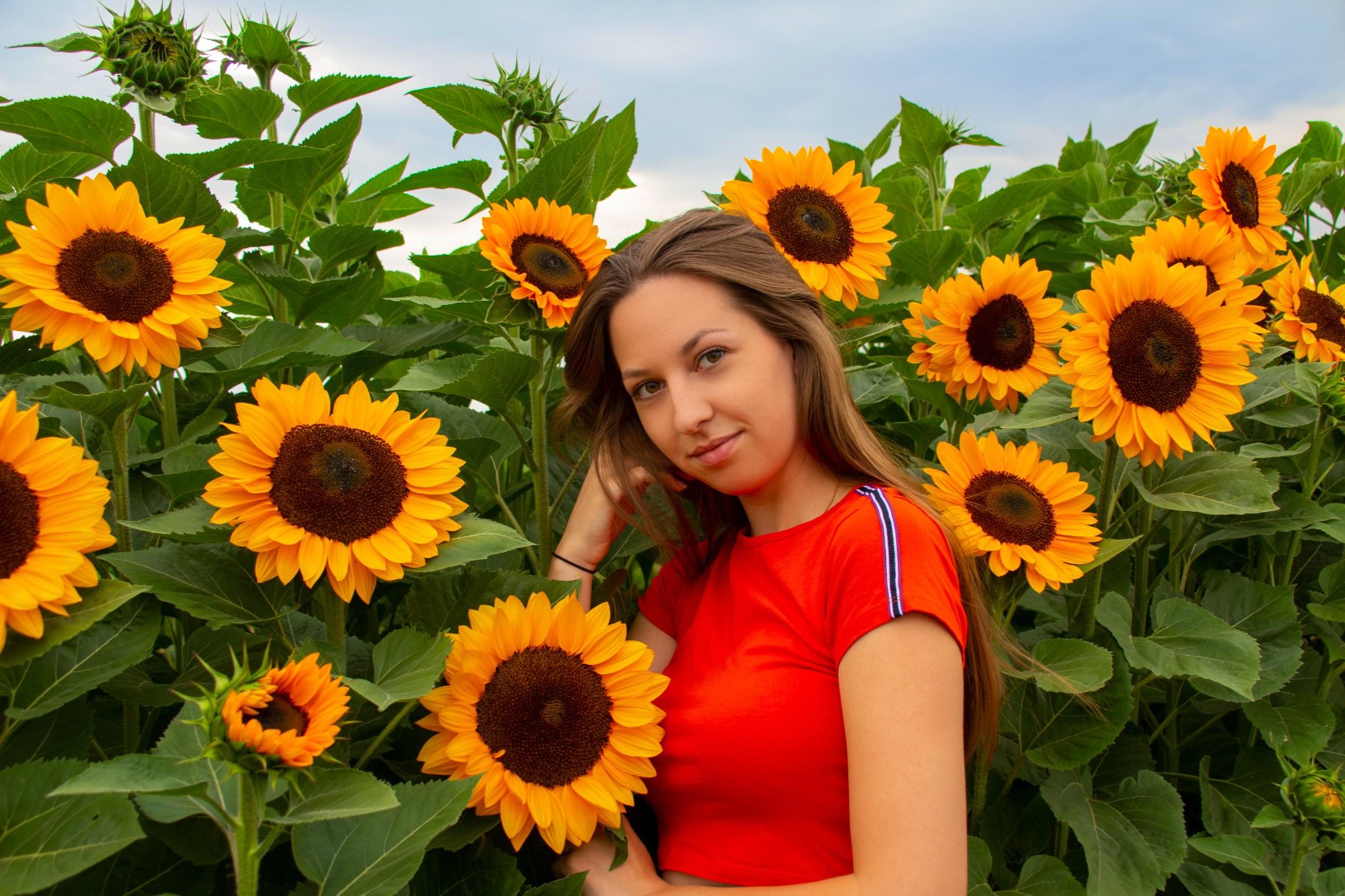 Junge Frau in orangefarbenem Top steht lächelnd in einem Sonnenblumenfeld. Die Gründerin Laura von dem Kleinunternehmen LaNuFaktur aus Deutschland.